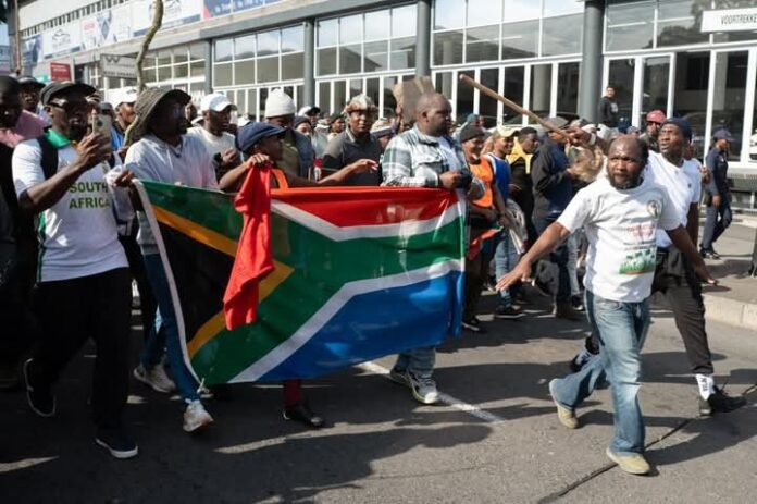 Demonstrators hold a South African flag as they march during a protest against undocumented migrants in Cape Town, South Africa on May 23, 2026 [Rodger Bosch/AFP]