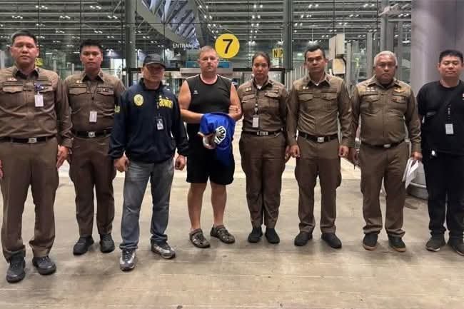 Simon Carman, 46, with Thai security personnel at the airport following his arrest 